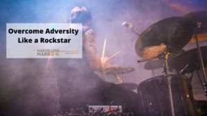 Drummer playing the drums with smoke in the air; Text reads, "overcome adversity like a rockstar" with Marvelless Mark's Motivational Speaker Logo underneath.